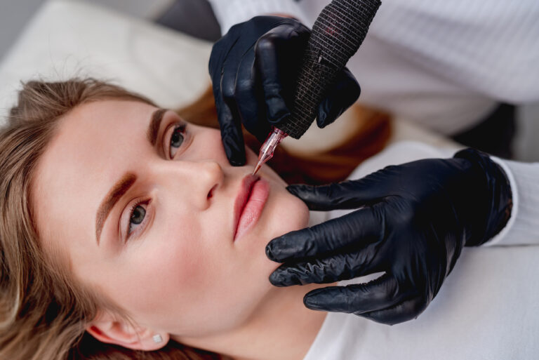 Permanent makeup master conturing lips in beauty salon. Side closeup view of tattoo process